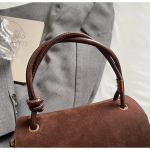 Detail of a brown suede bag featuring a woven knotted handle and vintage metal eyelets