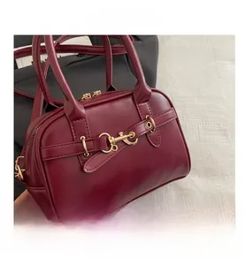 Close-up of burgundy leather handbag featuring gold metallic buckles and top handles