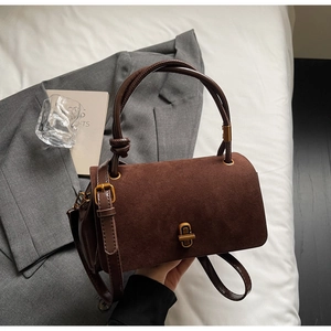 Detail of dark brown suede handbag with metal twist lock on a neutral fabric background