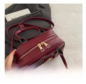 Detail view of burgundy handbag featuring smooth dual gold zippers and matte leather texture