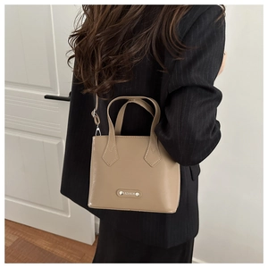 Detail of camel bucket bag with metal logo, held by model in black striped blazer