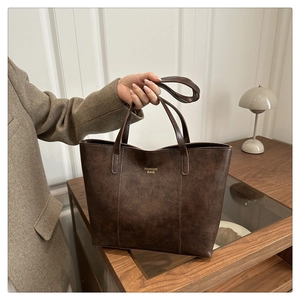 Détail macro du sac cabas marron foncé montrant la texture mate et l'écrit doré