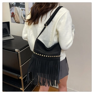 Detail of black suede tassel bag featuring gold pyramid studs and adjustable shoulder strap