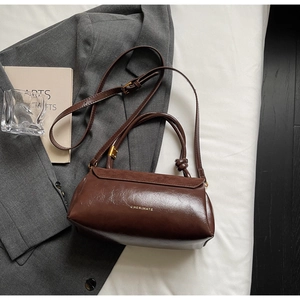 Close-up of deep brown oil-wax leather texture with gold logo on suede crossbody bag