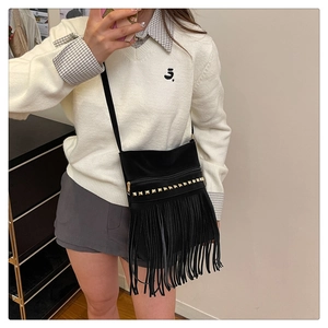 Détail du sac bandoulière noir mat avec des rivets dorés et de longues franges souples