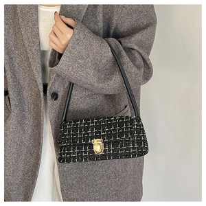 Close-up of black and gold tweed underarm bag with metallic twist lock on tweed blazer