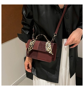 Detail of burgundy crossbody bag with leopard print scarf handle worn by model