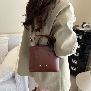 Minimalist deep brown bucket bag with gold fashion plaque and adjustable shoulder strap