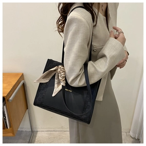 Detail of black leather tote bag featuring gold logo and decorative printed silk scarf