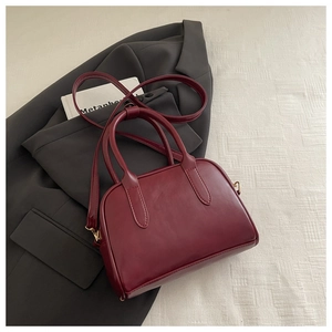 Detail of vintage burgundy leather handbag with dual handles on a grey blazer