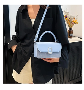 Détail du sac bandoulière bleu clair avec texture tissée et boucle sur chemise noire