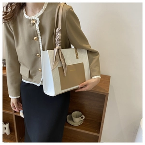 Detail of a two-tone woven tote bag with a brown leather pocket and silk scarf handle