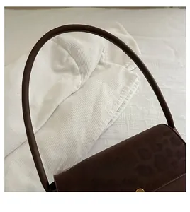 Detail of dark brown leather handbag featuring a leopard print flap and gold metal buckle
