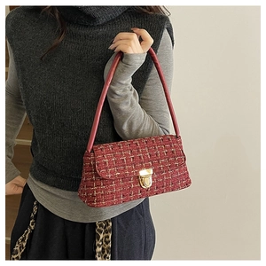 Detail of red tweed shoulder bag with golden lock and leather strap worn by a model