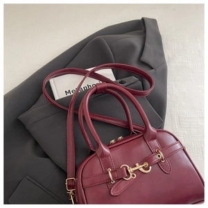 Detail of burgundy leather handbag with gold metal buckle on a dark grey blazer