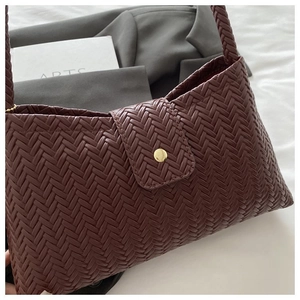 Detailed view of burgundy woven texture on shoulder bag with a gold metal button clasp