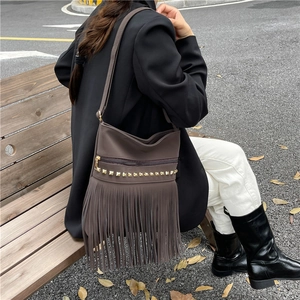 Vintage brown tassel bucket bag with gold studs in a casual outdoor lifestyle setting