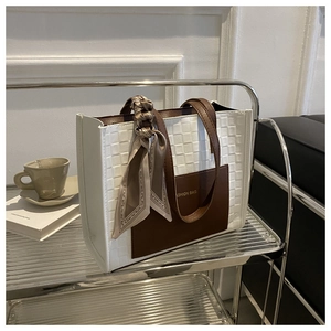 Detail of checkered tote bag with fashion text and silk scarf on a modern glass shelf