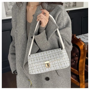Detail of white tweed underarm bag with gold clasp and leather strap on model