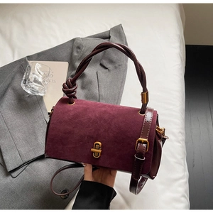 Detail of burgundy suede handbag featuring a twisted handle and gold twist-lock closure