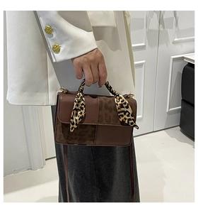 Detail of a brown leather crossbody bag with leopard print accent and silk scarf handle