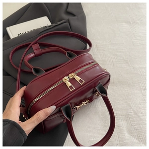 Close-up of vintage wine red handbag with dual golden zippers and matte leather texture