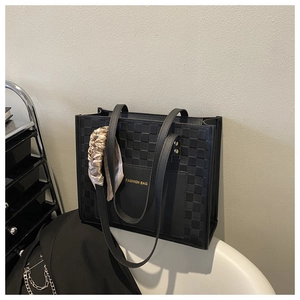 Detail of black checkered tote bag with gold logo and elegant satin ribbon decoration