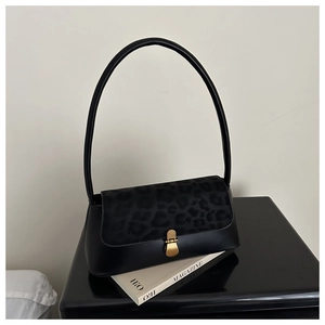 Close-up of retro black shoulder bag with leopard print flap and gold clasp on a magazine