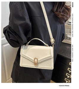 Detail view of white leather crossbody bag with golden metal clasp and adjustable strap