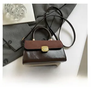 Detail of dark brown leather and suede handbag with gold buckle and smartphone for scale