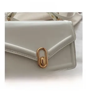 Close-up of a white matte leather handbag with a golden oval twist lock and V-shaped flap