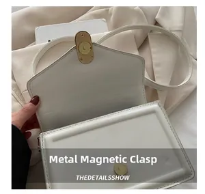 Close-up of white leather handbag featuring a golden circular magnetic snap closure