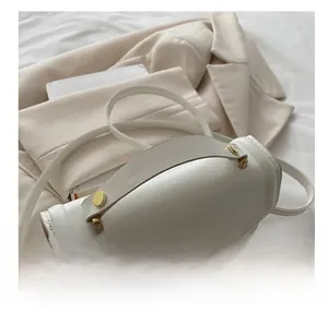 Close-up of white leather handbag featuring gold metal rivets and a swivel lock closure