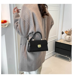 Polished black leather crossbody bag with golden buckle styled on a wool coat
