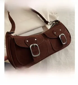 Détail du sac porté épaule en daim marron avec deux poches à rabat et boucles argentées