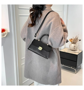 Detail of black textured crossbody bag with gold square clasp and round top handle