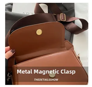 Detail of the golden magnetic metal closure on the brown leather saddle bag interior
