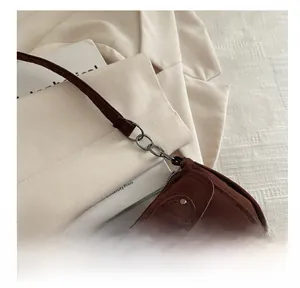 Détail d'un sac bandoulière en daim marron avec boucles métalliques et finitions de sangle