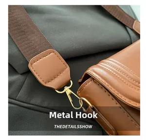Close-up of golden metal swivel hook and textured fabric strap on brown leather saddle bag