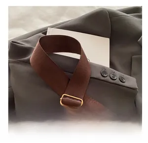 Detail view of adjustable wide woven shoulder strap with gold buckle on a brown saddle bag