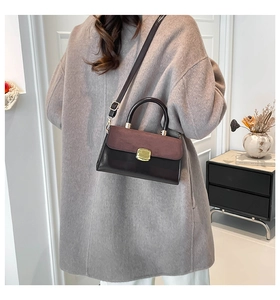 Detail of a brown leather and red suede crossbody bag with gold buckle on a model