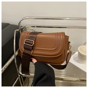 Close-up of brown PU leather saddle bag with wide fabric strap on a metal display stand