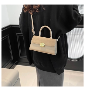 Detail of beige square handbag featuring suede flap and gold buckle worn as crossbody