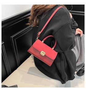 Detail of red leather crossbody bag featuring matte flap and golden metal lock hardware