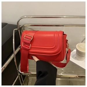 Detail of red leather crossbody bag with curved stitching on a metallic shelf
