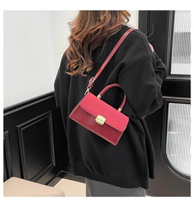 Detail of red and burgundy contrast handbag with gold hardware and top handle shown on shoulder