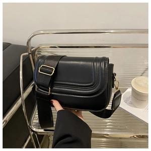 Close-up of black leather saddle bag with gold hardware and wide woven shoulder strap