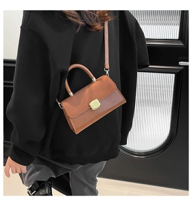 Close-up of caramel PU leather handbag with gold clasp worn as a shoulder bag