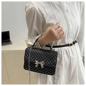 Detail of grey dotted small square bag with silver bow ornament and metal chain strap