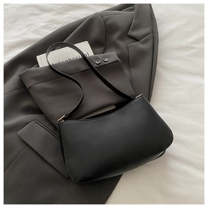 Close-up of minimalist black matte leather underarm bag with gold hardware on a suit jacket